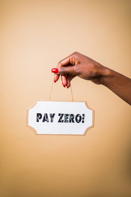 A close-up of a woman's hand with red nail polish holding a small string, hanging a white sign with a decorative border that reads 'PAY ZERO!'. The hand is positioned against a plain beige background.